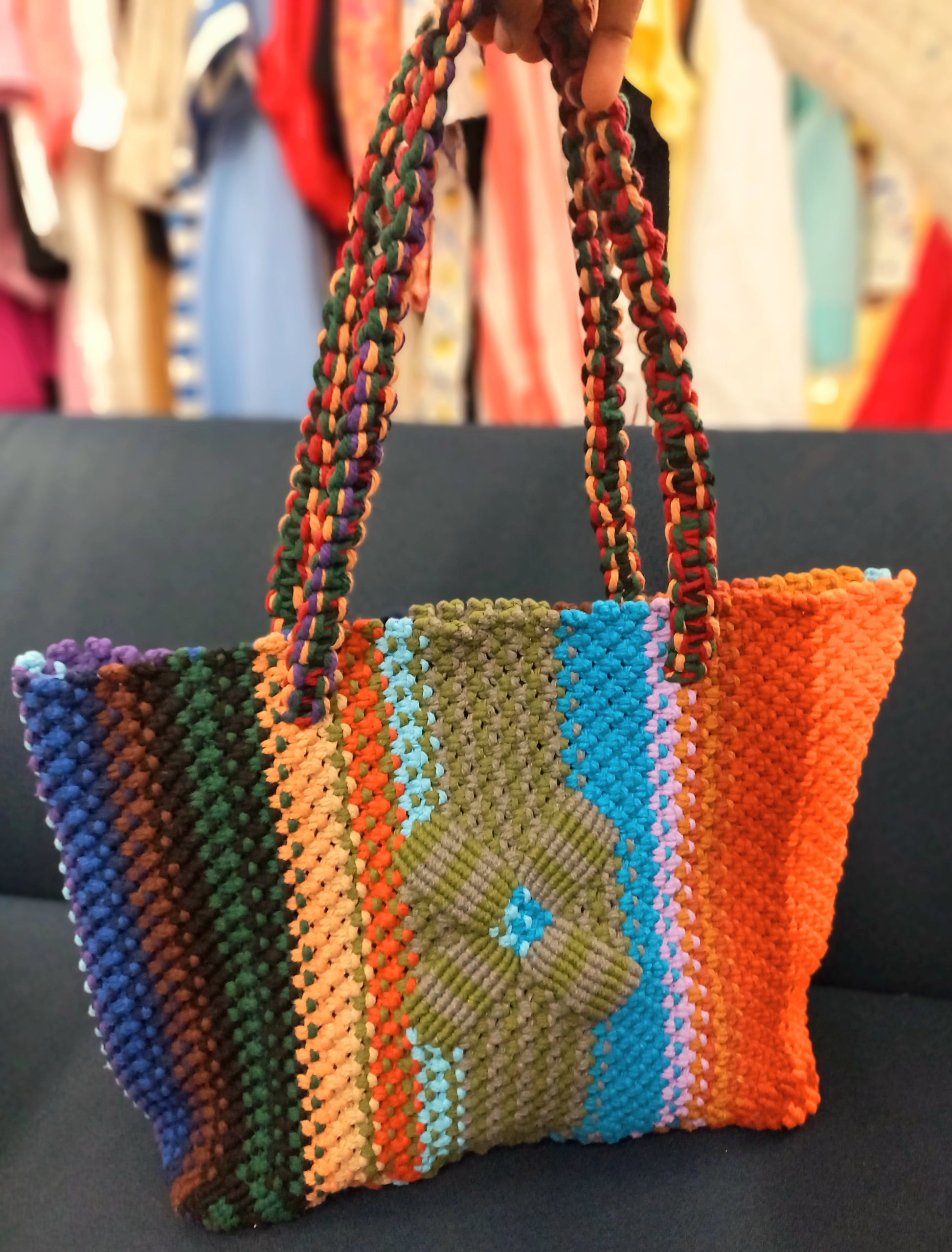 Colorful woven handbag with a floral design held against a clothing store background.