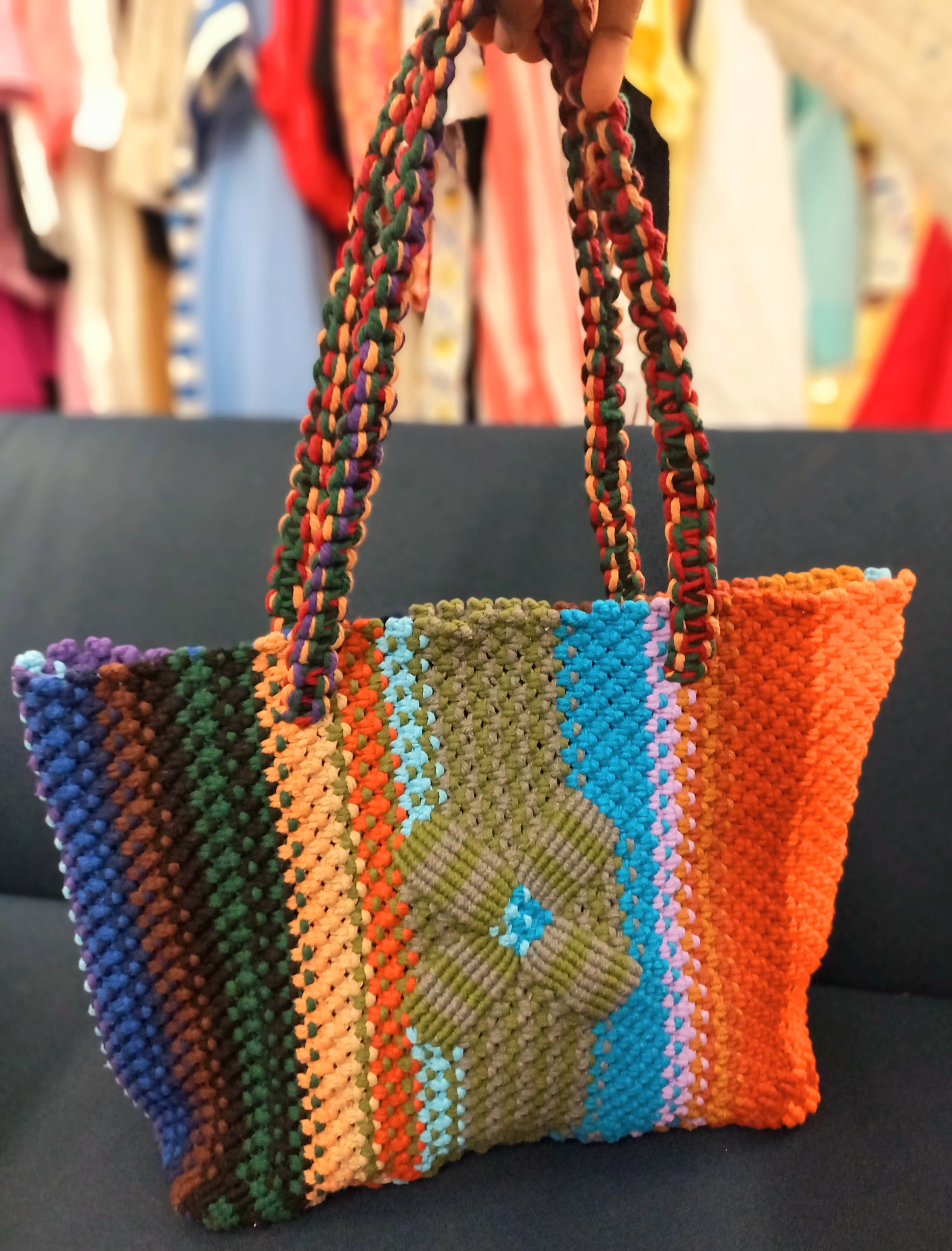 Colorful woven handbag with a floral design held against a clothing store background.